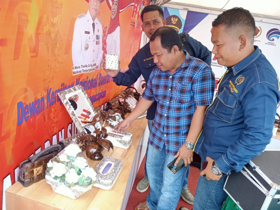 Kasi Informasi Publik Pemko Tanjungbalai Dedi Simorangkir AMd didampingi anggota PWI Tanjungbalai menunjukkan hasil kerajinan kulit kerang, di stan Pemko Tanjungbalai saat HPN di Medan.