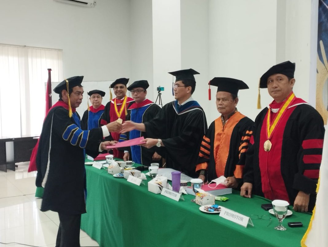 Dr Layari Sinukaban MTh saat menerima hasil disertasinya yang diserahkan Ketua Sidang Dr Endro Tobing MHum disaksikan Sekretaris Dr Suardin Gaurifa MTh, Promotor Dr Ir Ferlin Zebua MM, Dr Robert Benediktus MA MTh, Prof Dr Benyamin Situmorang, Penguji Dr Stevanus Liong MTh dan Dr Saur Hasugian MTh, dalam sidang terbuka promosi doktoral yang dilaksanakan di STTPK GBI Rumah Persembahan Sumatera Resort Jalan Jamin Ginting Medan.