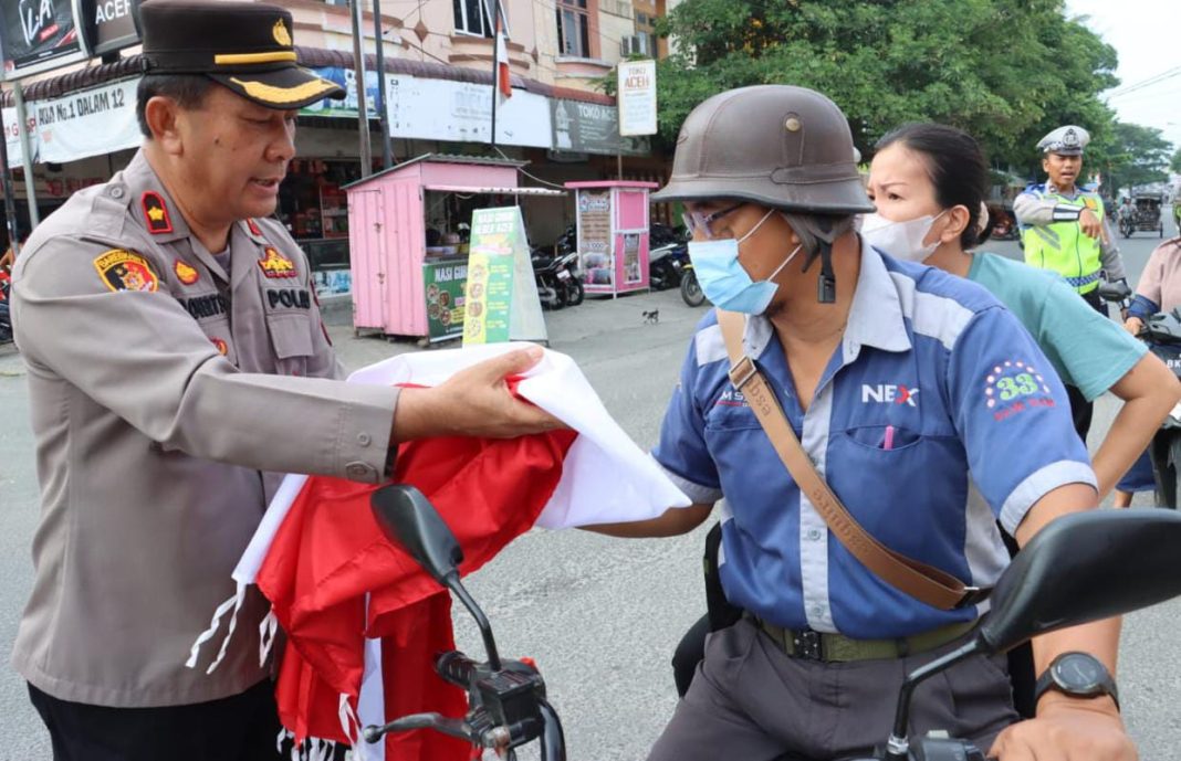 Wakapolres Tebingtinggi Kompol Asrul Robert Sembiring SH MH membagikan bendera Merah Putih kepada warga yang melintas di depan Mapolres setempat, Jalan Pahlawan, Jumat (4/8/2023).