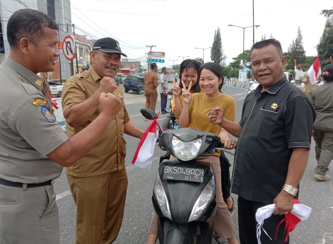 Anggota DPRD Simalungun Jon Redikalmen Sidauruk (kanan) bersama Kepala Kesbangpol Simalungun Arifin Nainggolan memasang bendera merah putih pada kendaraan masyarakat di Pamatangraya, Selasa (8/8/2023).