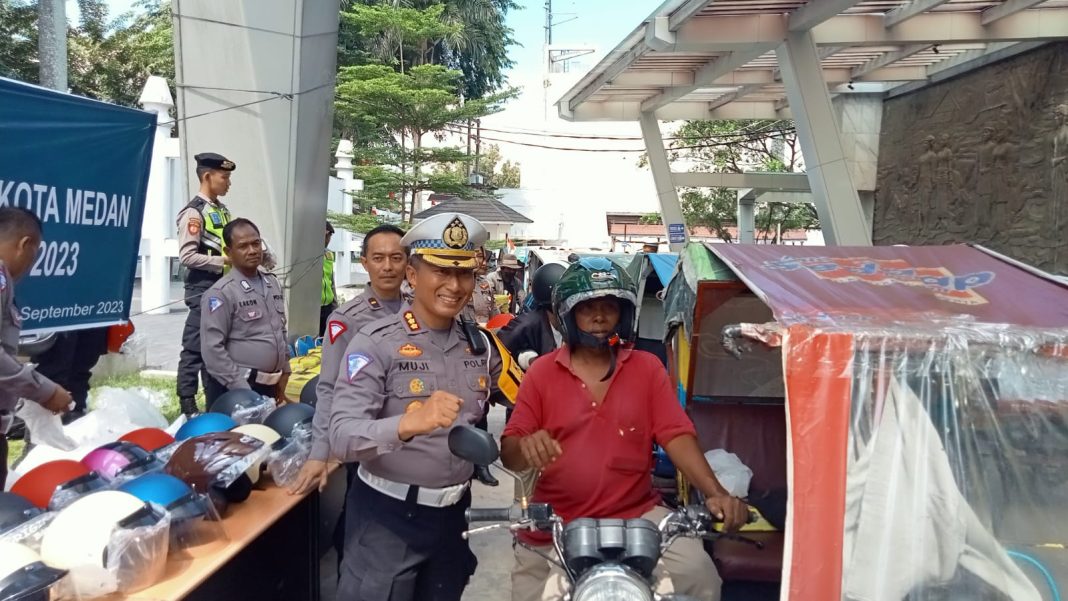 Direktur Lantas Polda Sumut Kombes Pol Muji Ediyanto membagikan helm SNI ke abang betor, Senin (11/9/2023). (Dok/Polda Sumut)