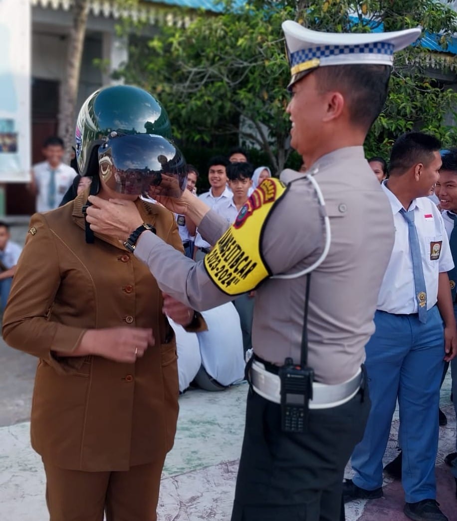 Kasat Lantas Polres Pelabuhan Belawan mengenakan helm kepada salah seorang guru SMAN 20 Medan pada kegiatan Police Goes to School, Senin (29/1/2024). (Dok/Polres Belawan)