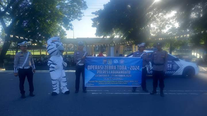 Tim Satlantas Polres Labuhanbatu bersama badut zebra membentang spanduk ke arah pengendara, saat sosialisasi Operasi Zebra Toba 2024, di Jalan MH Thamrin Rantauprapat, Sabtu (19/10/2024).