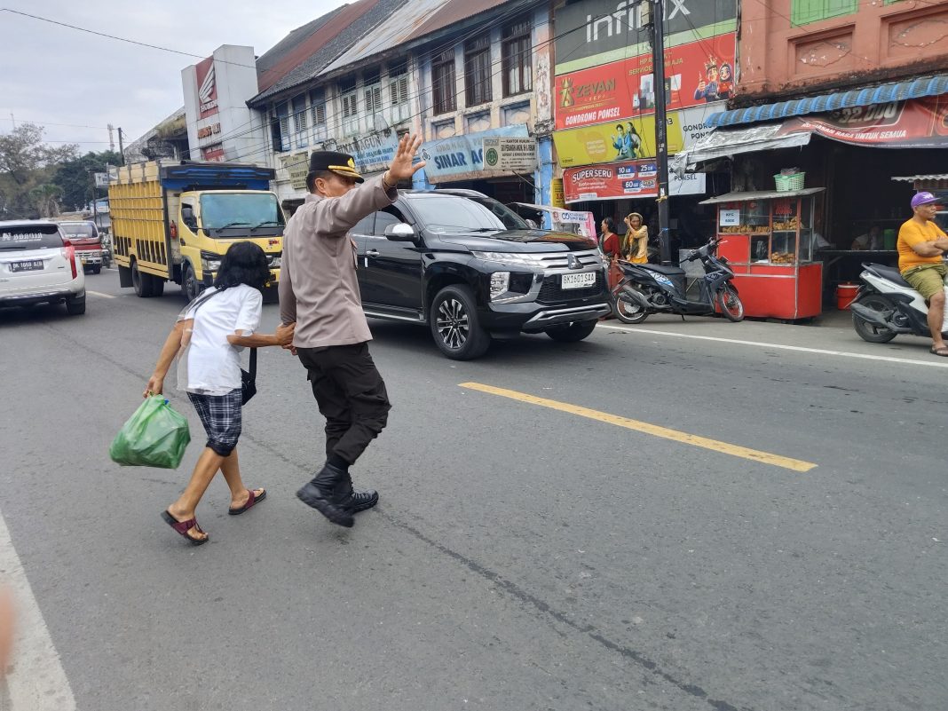 Kapolsek Pancurbatu Kompol H Djanuarsa SH Djanuarsa sedang membantu warga menyeberang jalan saat melakukan pengaturan lalu lintas di depan Pasar Pancurbatu, yang terletak di Jalan Letjen Jamin Ginting, Sabtu (15/2/2025). (Dok/Polsek Pancurbatu)