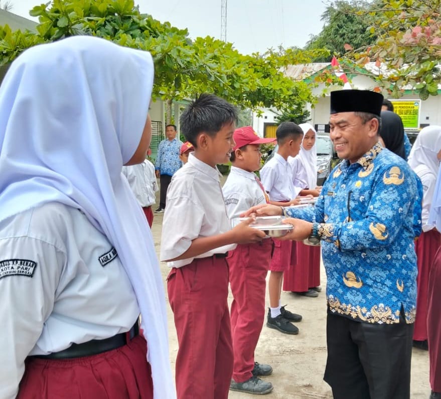 Kadisdik Sergai, Suwanto Nasution diwakili Sekretaris Agus Salim Berutu, membagikan MBG ke pelajar saat launching perdana di Kecamatan Pantaicermin, Senin (17/2/2025). (Dok/Disdik Sergai)