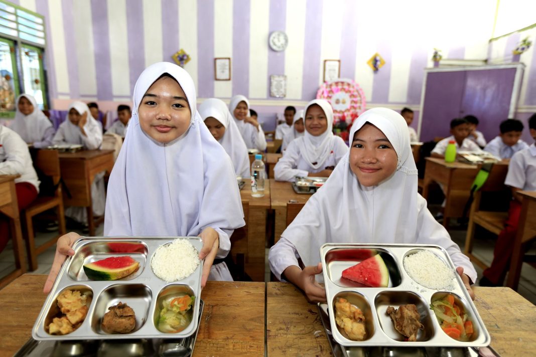 Dua siswi sekolah dasar menunjukkan paket makanan bergizi gratis yang mereka terima melalui program Makan Bergizi Gratis (MBG). (Dok/Kemenkeu)